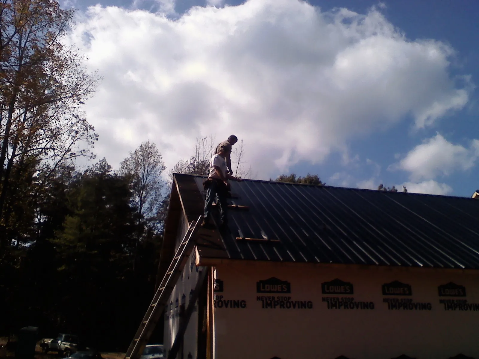 Roofer fastening dark metal panels high against a cloudy sky, from a Roof Inspection job in Alapaha