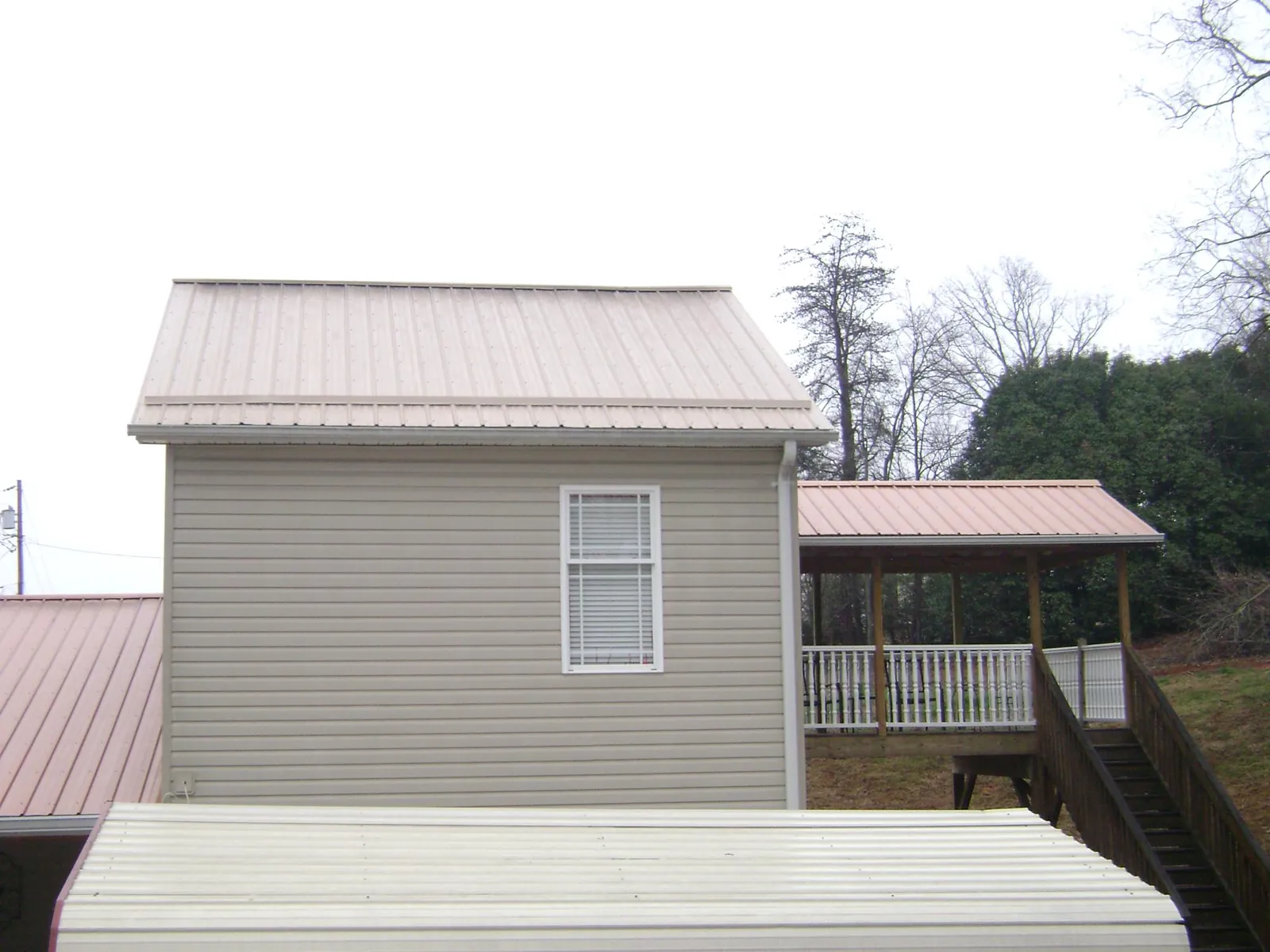 Tan metal roofs on a two story addition and attached porch, from a Roof Replacement job in Alapaha